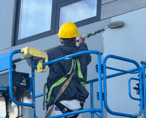 Man With Paint Roller Coating Building Exterior