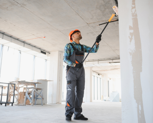 Construction Worker Painting Walls And Ceiling With Telescopic Paint Roller