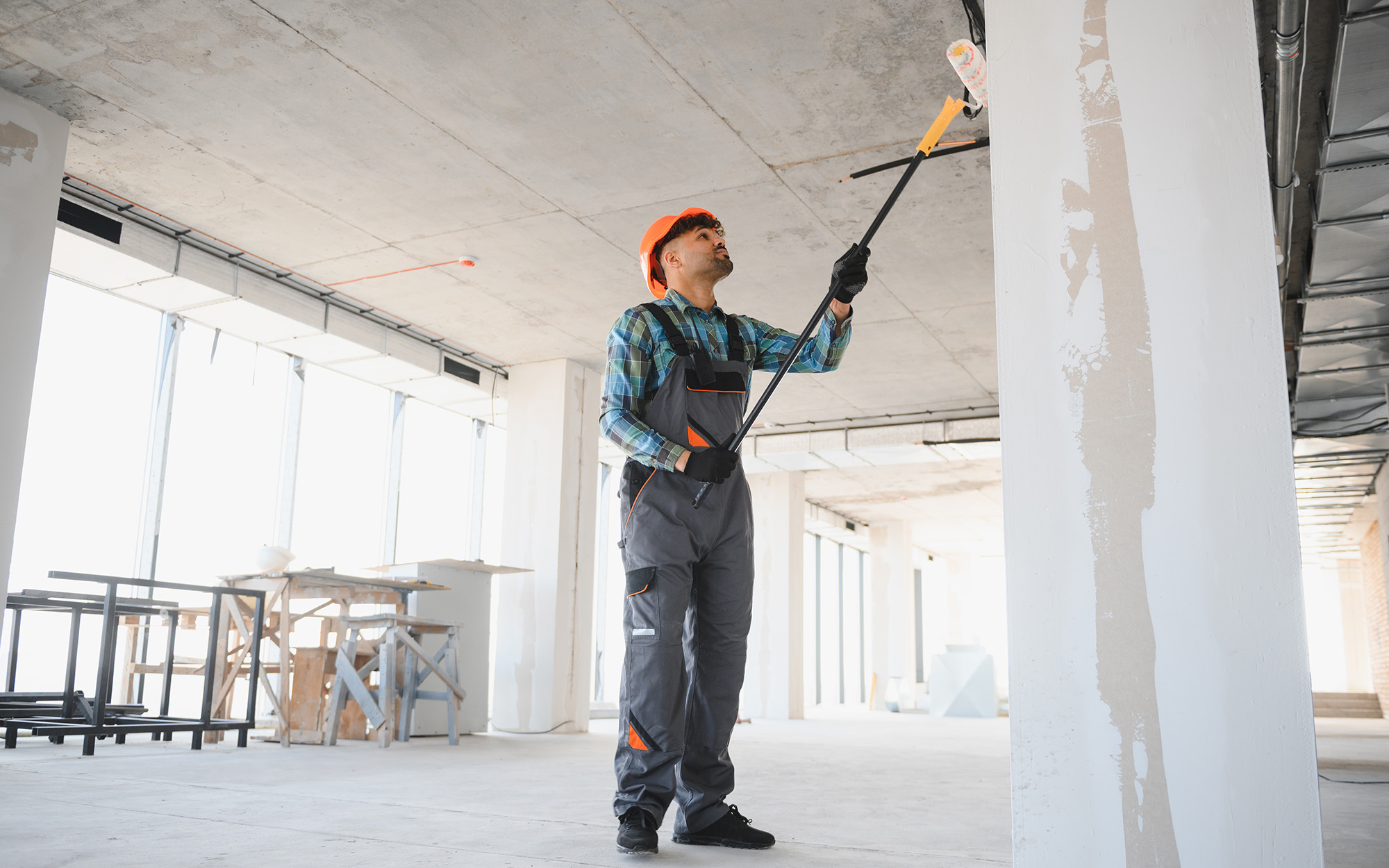 Construction Worker Painting Walls And Ceiling With Telescopic Paint Roller